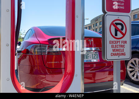Tesla Model S rouge garée, charge chez Tesla Supercharger avec parking minimal à l'arrière du véhicule. Banque D'Images