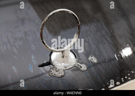 Gros plan sur l'emblème d'un ca sur le capot d'une voiture noire pendant le lavage et le nettoyage dans le détail atelier avec de l'eau et du savon en mousse Banque D'Images