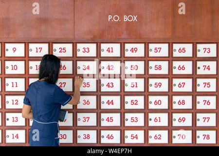 Une jeune femme ouvre boîte aux lettres sur mur plein de boîtes aux lettres. Femme à l'aide de boîtes de dépôt sur le mur. Banque D'Images