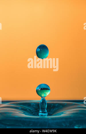 Goutte d'eau, bleu goutte d'eau, de l'eau splash close-up isolé sur fond orange, beaucoup de bulles, liquid motion Banque D'Images