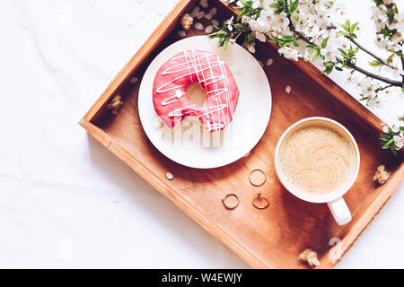 Printemps brealfast au lit. Plateau avec strawberry donut rose avec café et fleur de printemps. Girl reading a book. Vue d'en haut. Copier l'espace. Banque D'Images