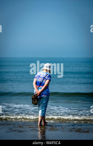 Femme marchant le long d'une plage de sable fin avec la mer et le ciel bleu Banque D'Images