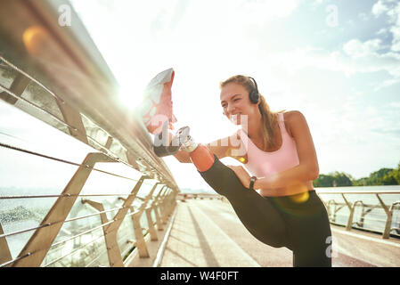 Une femme handicapée dans les vêtements de sport et d'écouteurs stretching prothèse en étant debout sur le pont. L'écoute de la musique. Mobilité sport concept. La motivation. Mode de vie sain Banque D'Images