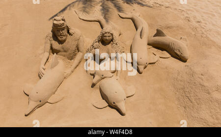 Sculpture de sable d'un homme et femme avec les dauphins sur la plage de sable Banque D'Images