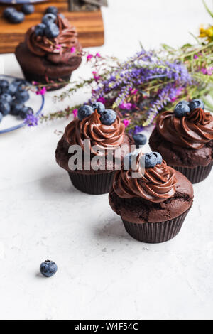 Des petits gâteaux au chocolat avec crème au beurre et les bleuets sur tableau blanc, bouquet de fleurs sauvages, Close up, délicieux dessert de fête Banque D'Images