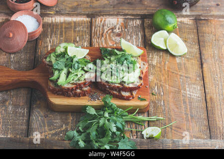 Toasts à l'avocat avec la coriandre et citron vert, à base de plantes en bonne santé des sandwichs, table en bois en milieu rural, l'heure du goûter Banque D'Images
