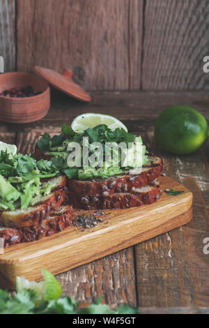 Toasts à l'avocat avec la coriandre et citron vert, à base de plantes en bonne santé des sandwichs, table en bois en milieu rural, l'heure du goûter Banque D'Images