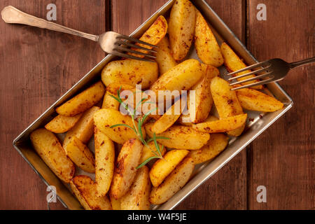 Les quartiers de pommes de terre rôties au four, avec du romarin, dans une plaque de cuisson sur un fond sombre, rustique en bois tourné d'en haut Banque D'Images