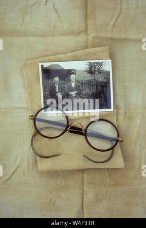 Lunettes avec verres antiques circulaire et cadres fil couché sur les vitraux et le linge plié avec photo en noir et blanc de personnes âgées 1940 couple Banque D'Images