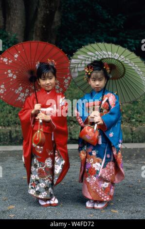 Le Japon, Honshu, Tokyo, deux jeunes filles habillées en kimono traditionnel Papier Holding parasols pour l'assemblée annuelle 7-5-3 (Shichi-go-san) a tenu le 15 novembre Banque D'Images