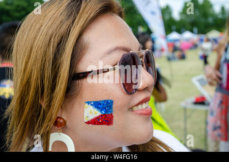 Une dame portant des lunettes de soleil avec le drapeau des Philippines peint avec la peinture pour le visage et des paillettes sur sa joue. Banque D'Images