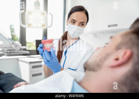 Female dentist holding échantillons mâchoire dent avec accolades modèle. Clinique dentaire professionnel. Banque D'Images