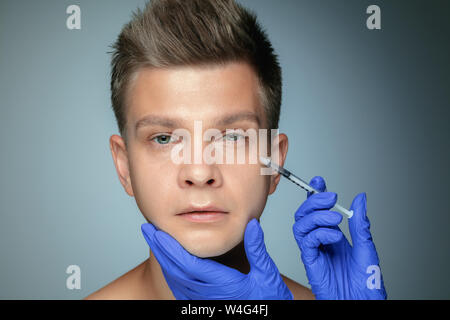 Close-up portrait of young man isolé sur fond studio gris. Procédure de chirurgie de remplissage. Concept de l'Homme de santé et beauté, cosmétologie, auto-soins, soins du corps et de la peau. Anti-vieillissement. Banque D'Images