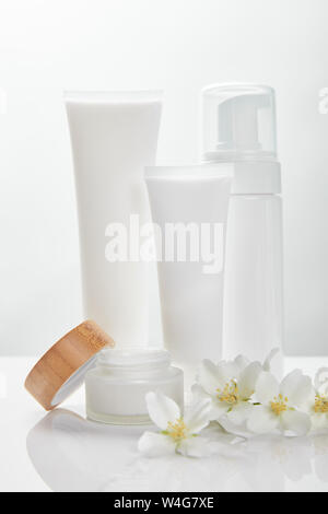 Fleurs de jasmin sur surface blanche près de la crème dans les tubes, jar et distributeur de cosmétiques Banque D'Images