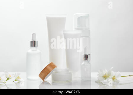 Fleurs de jasmin sur surface blanche près de bouteilles en verre, la crème en tube, jar et distributeur de cosmétiques Banque D'Images