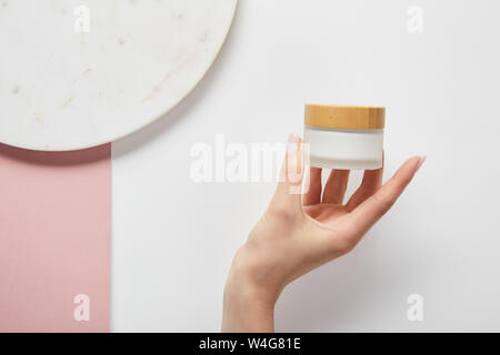 Portrait de femme tenant à la crème pot près de la plaque sur la surface blanche rose Banque D'Images