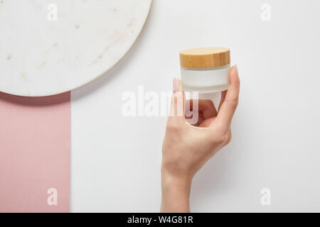 Portrait de femme tenant à la crème pot près de la plaque sur la surface blanche rose Banque D'Images