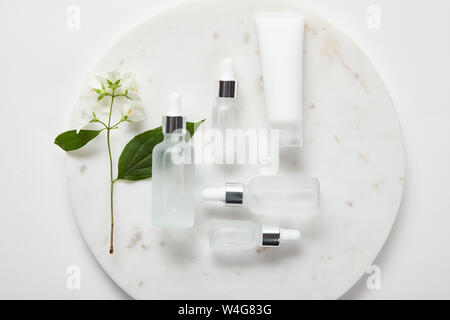 Vue de dessus du tube de crème et des bouteilles en verre en plaque avec jasmine sur surface blanche Banque D'Images