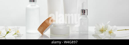 Vue panoramique tourné de crème en tube, jar et cosmétiques bouteilles en verre avec surface blanche sur jasmine Banque D'Images