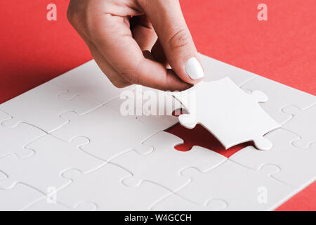 Portrait of woman holding white jigsaw près de pièces de puzzle connecté sur rouge Banque D'Images