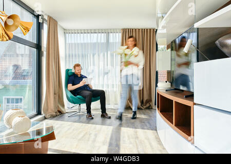 Couple à la maison, l'homme à l'écoute de la musique, femme portant vase avec fleurs Banque D'Images