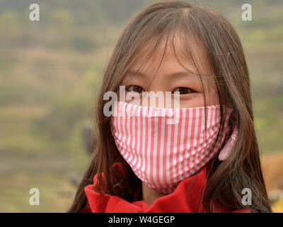 Jeune femme vietnamienne avec de beaux yeux orientaux lui couvre le nez et la bouche avec un masque de protection à rayures. Banque D'Images