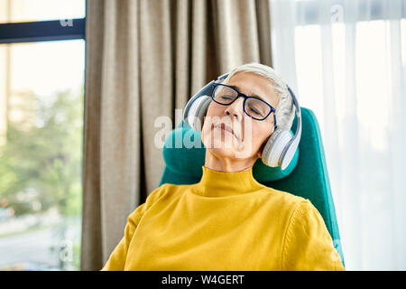 Senior woman sleeping in fauteuil avec écouteurs Banque D'Images