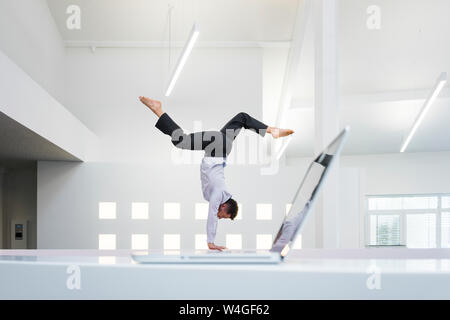 Businessman doing a handstand at laptop in office Banque D'Images