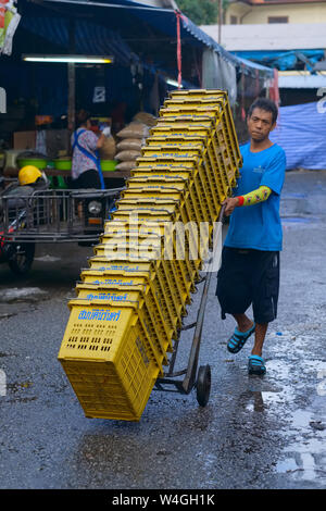 Un travailleur migrant du Myanmar (Birmanie) dans un marché en Thaïlande, le transport de caisses en plastique empilées ; Lieu : La ville de Phuket, Thaïlande Banque D'Images