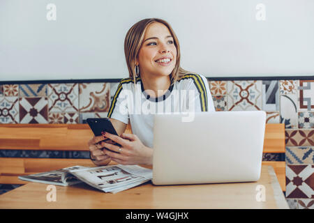 Jeune femme en utilisant le téléphone mobile et l'ordinateur portable en cafe Banque D'Images