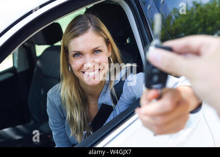 Portrait of smiling young woman looking at camera while holding car keys et le donner à quelqu'un par la fenêtre Banque D'Images