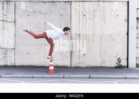 Jeune homme en équilibre sur le cône de la circulation en face de mur de béton Banque D'Images