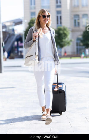 Young businesswoman looking at camera while walking with suitcase Banque D'Images