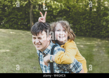 A smiling girl riding sur le dos de son grand frère Banque D'Images