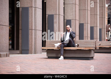 Businessman on the phone sitting on bench eating donut, New York City, USA Banque D'Images