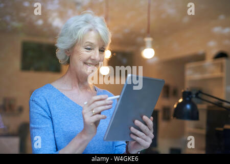 Portrait of smiling mature woman derrière la vitre using digital tablet Banque D'Images