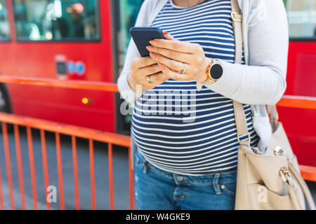 Femme enceinte en utilisant son téléphone à l'extérieur Banque D'Images