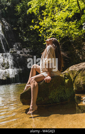 Jeune femme assise sur un rocher dans une chute, Garrotxa, Espagne Banque D'Images