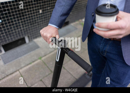 Businessman with E-scooter et café à emporter, vue partielle Banque D'Images