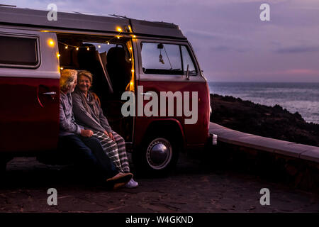 Senior couple voyageant dans un van, regardant le coucher du soleil au bord de la mer Banque D'Images