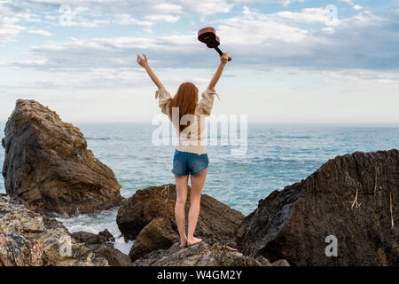 Vue arrière de jeune femme avec ukulele debout sur la roche face à la mer Banque D'Images