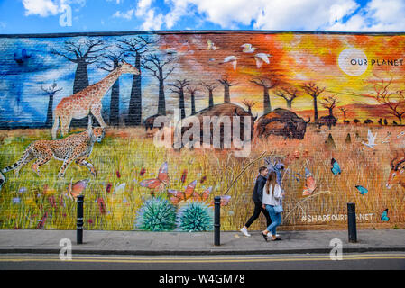 Les gens qui passent par le mur de graffiti art à Brick Lane Market à Londres, Royaume-Uni Banque D'Images