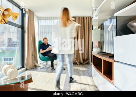 Couple à la maison, l'homme à l'écoute de la musique, femme portant vase avec fleurs Banque D'Images