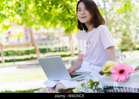 Jeune femme avec un ordinateur portable et d'écouteurs un pique-nique dans le parc Banque D'Images
