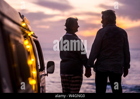 Senior couple voyageant dans un van, regardant le coucher du soleil au bord de la mer Banque D'Images