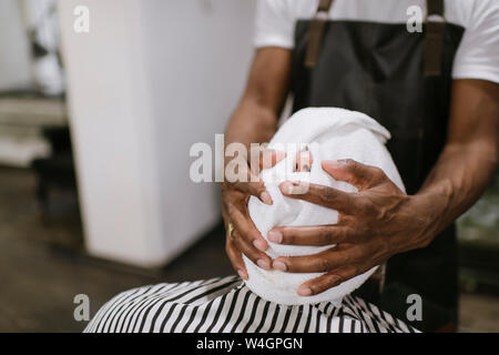 Coiffure L'essuyant le visage du client avec une serviette chaude dans barber shop Banque D'Images