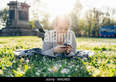 Smiling young woman lying on a meadow à rétro-éclairage looking at cell phone Banque D'Images