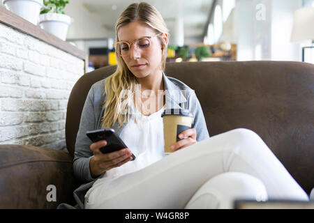 Jeune femme textos avec son téléphone portable tout en buvant un café dans un café Banque D'Images