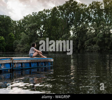 Relaxed woman sitting on jetty à un lac éloigné Banque D'Images