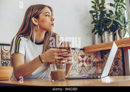 Jeune femme en utilisant le téléphone mobile et l'ordinateur portable en cafe Banque D'Images